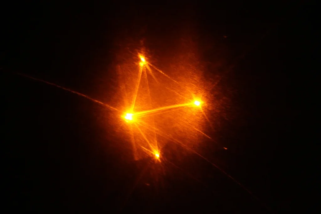 Gelb-orangefarbene Laserlinien bilden ein Dreieck mit hellen Knotenpunkten – Lichtkunst mit Laser und Kristall, Theater der Schatten Bamberg